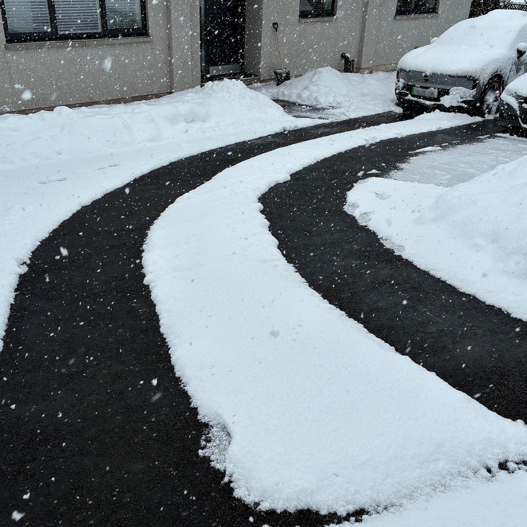 Snow-covered driveway and car in a residential area during a snowfall, with the snow melted from the Snowtec system