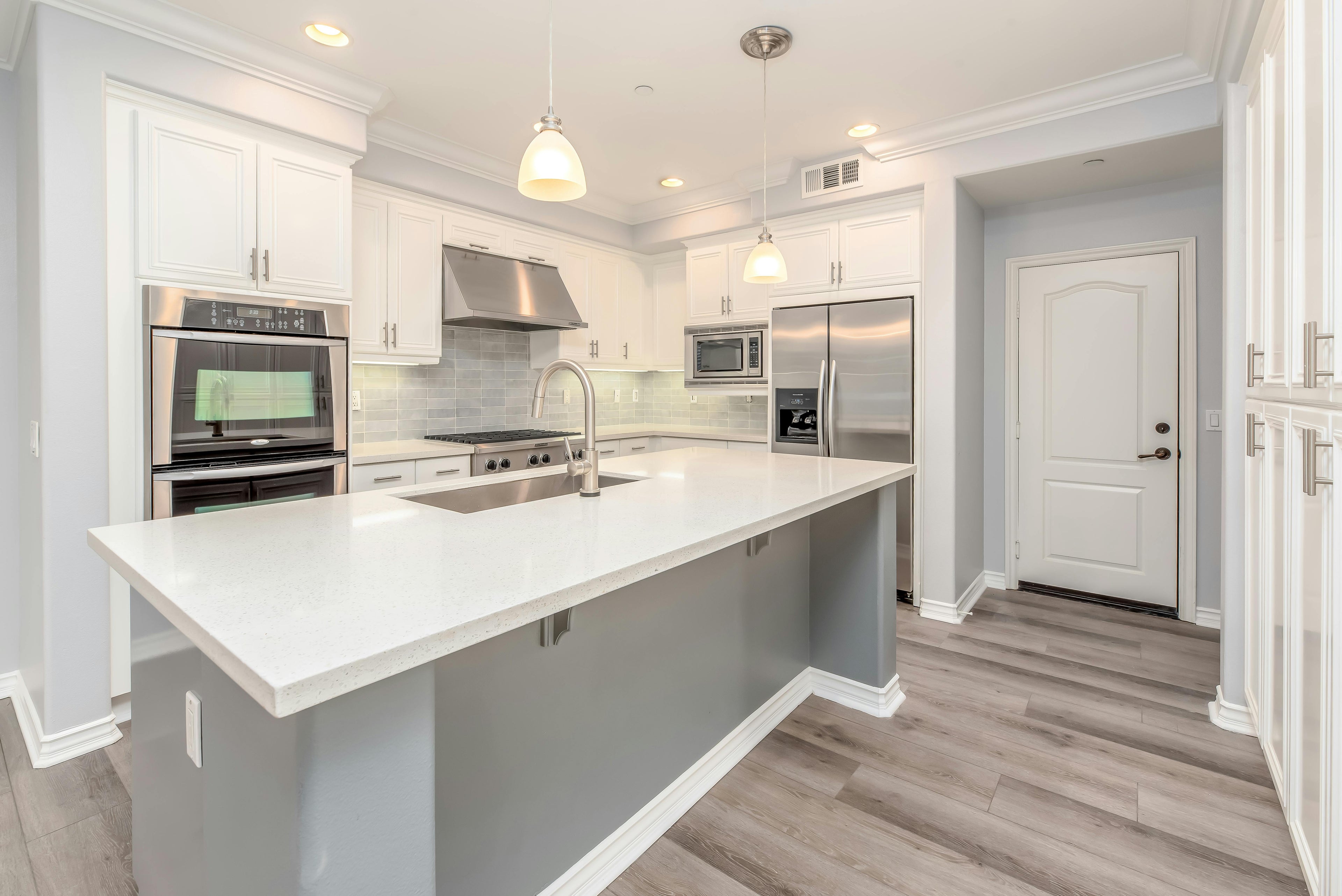 Modern kitchen with white countertops, stainless steel appliances, and gray island.